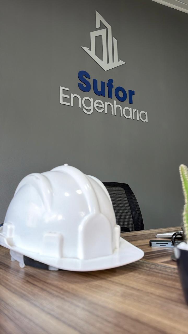 Capacete branco sobre a mesa no escritório da Sufor Engenharia, com o logo na parede